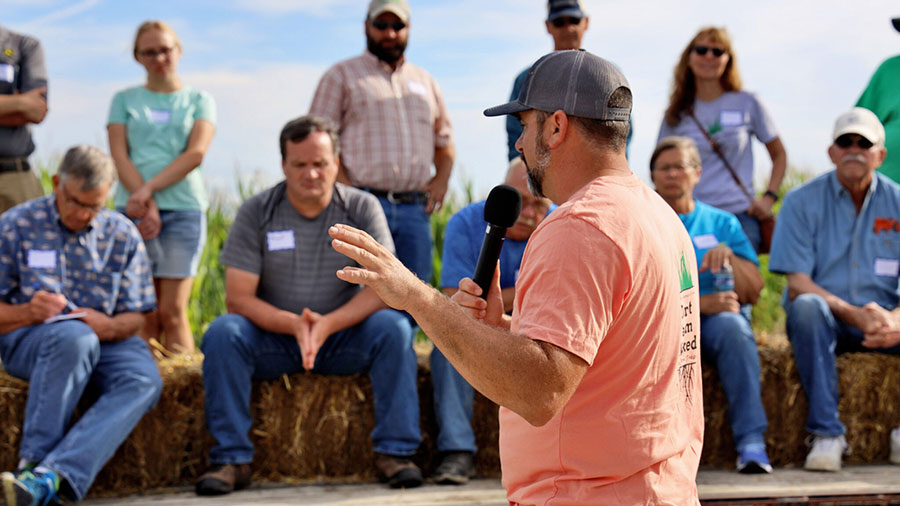 A man speaks into a microphone as he stands in front of a group of Iowa farmers. 