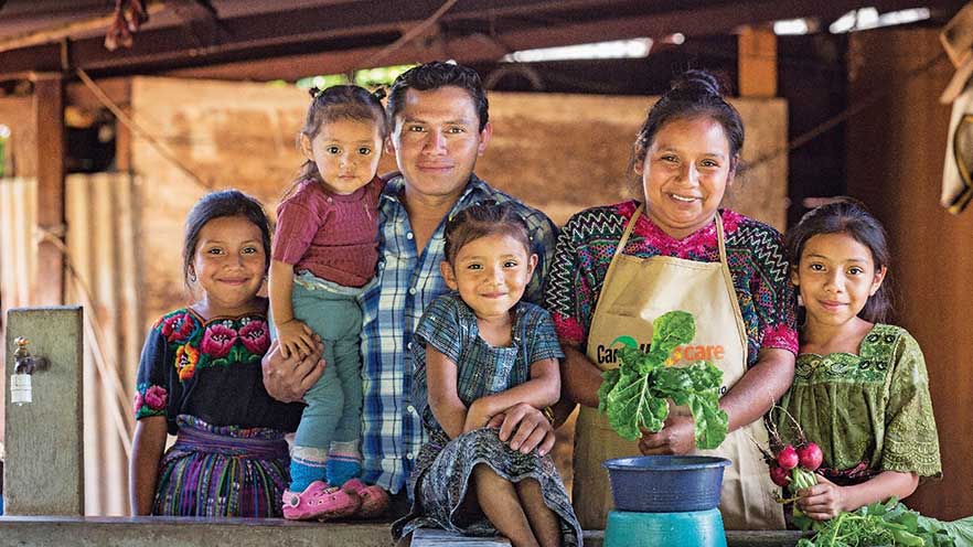 A woman and man stand with four children and hold vegetables in their hands. A woman and man stand with four children and hold vegetables in their hands.
