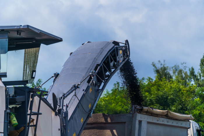 Asphalt milling machine loading recycled asphalt into a dump truck at a road construction site