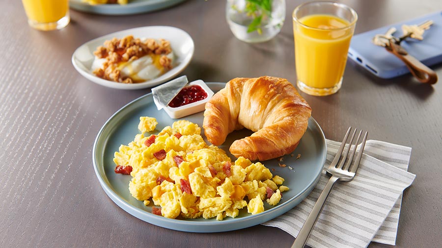 a plate on a table with eggs, bacon and a croissant.  