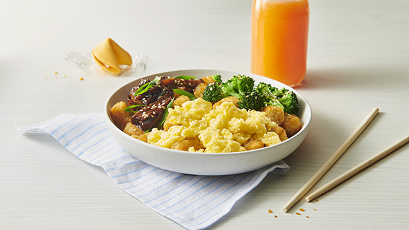 A white bowl with eggs, tater tots, broccoli and beef. 