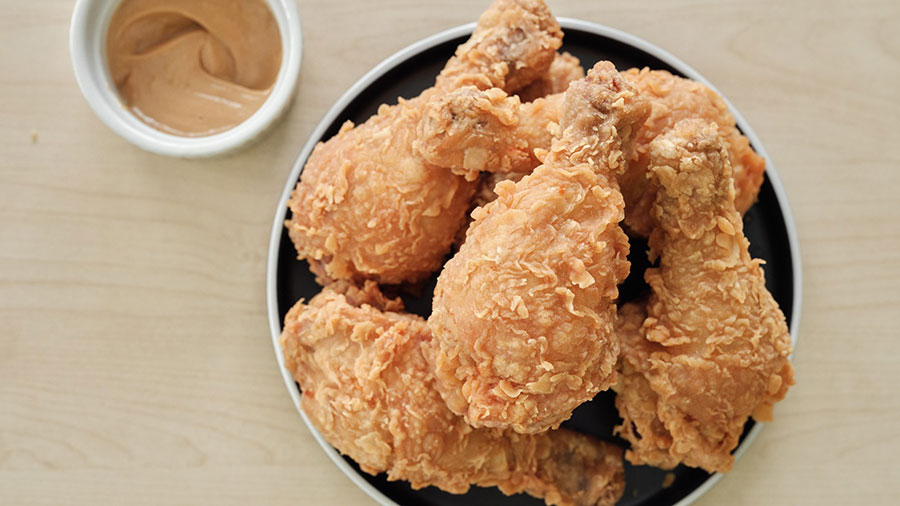 A bowl with five pieces of fried chicken on a brown table. A bowl with five pieces of fried chicken on a brown table.