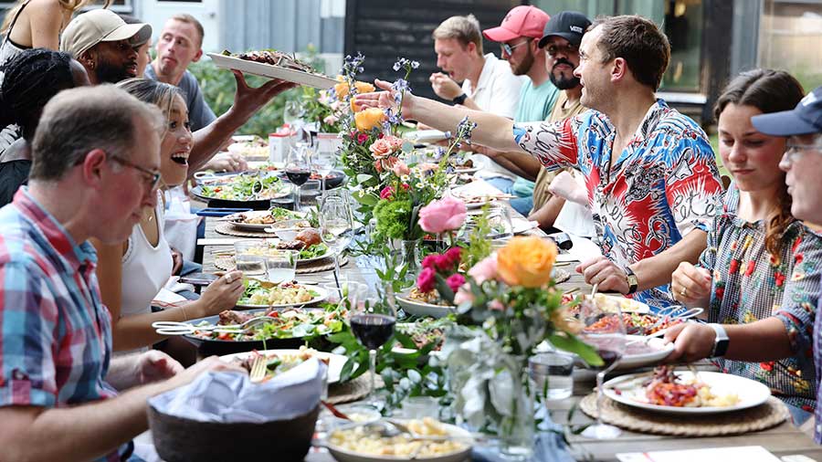 A group of 12 people sit at a large table laid with full plates of food. 