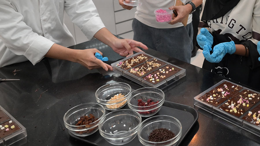 Three people stand above a counter filled with chocolate bars and several toppings, showing the kind of innovative chocolate solutions Cargill and customers pursue together. 