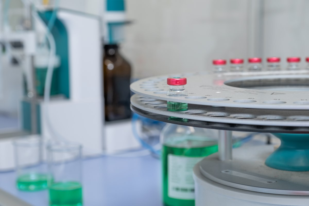 Close-up of laboratory equipment with small vials of green liquid on a rotating tray used for testing dielectric fluid.
