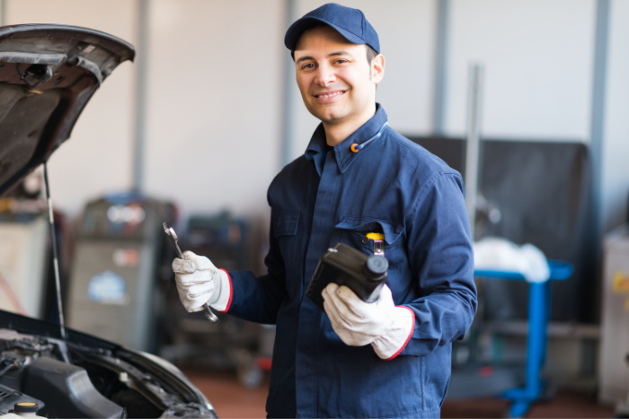 Portrait of an auto mechanic putting oil in a car engine