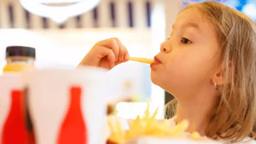 A little girl holds a French fry as she starts to take a bite.  