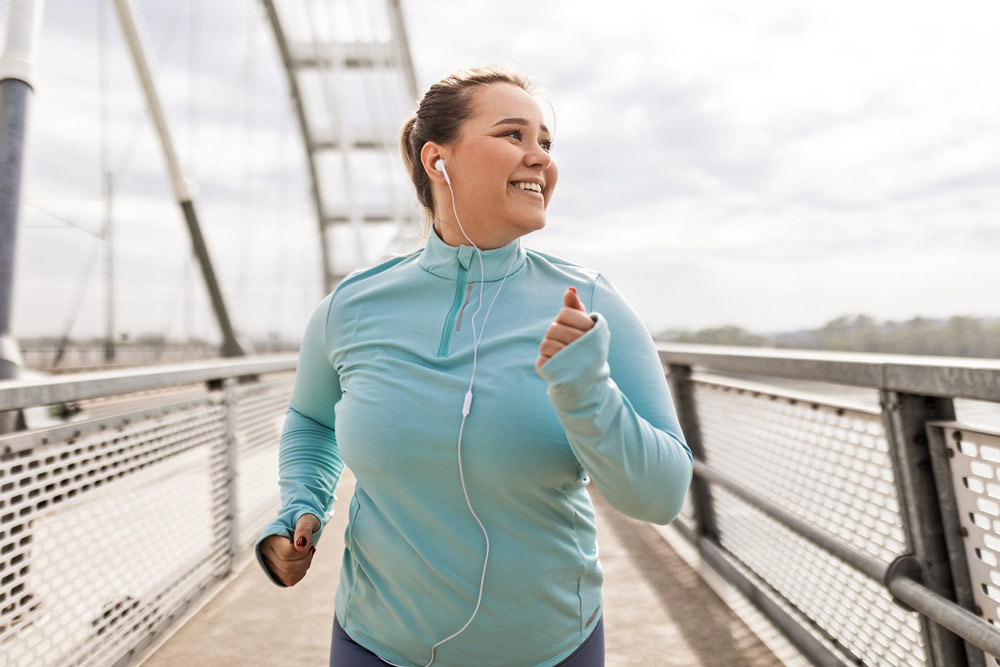 Person jogging outdoors on a pedestrian bridge while listening to music.