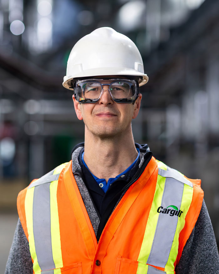 Employee wearing a hard hat, safety glasses and a high-visibility vest at an industrial facility.