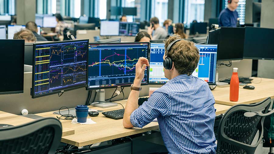 A male trader wearing headphones sits on the Cargill trading floor in front of three screens with graphs on them and moves his computer mouse. A male trader wearing headphones sits on the Cargill trading floor in front of three screens with graphs on them and moves his computer mouse.