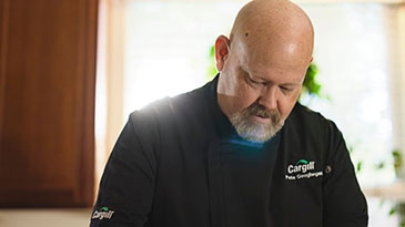 rgill chef Pete looks down at a dish while wearing a black Cargill shirt.  