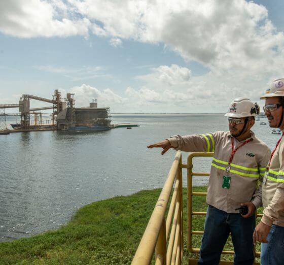Foto de dois funcionários da Cargill olhando para a mesma direção, tendo uma área portuária com uma instalação industrial